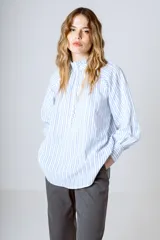 Blusa celeste con rayas verticales blancas, cuello mao y mangas largas abullonadas con puños elásticos.