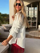 Camisa blanca con lunares negros, de mangas largas abullonadas con puños elastizados y cierre frontal con botones.