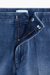 Jean de tiro alto con corte acampanado desde la rodilla. Confeccionado en denim con leve stretch, presenta cierre frontal con botón oculto y corchete, bolsillos traseros decorativos y pliegues frontales y posteriores.