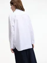 Camisa blanca de algodón con cuello camisero, cierre frontal con botones y apliques de pedrería en cuello y cartera de botones.
