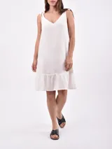 Vestido corto color crudo, de lino, con breteles finos con lazos y volado en el ruedo.