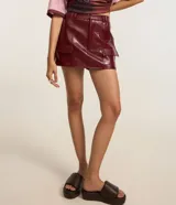 Short pollera de cuero sintético color bordó, con bolsillos delanteros con solapa y cierre frontal con cremallera.