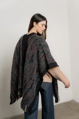 Ruana tejida color negro con diseño geométrico en blanco, celeste y rojo. Presenta cuello abierto y flecos en el ruedo.