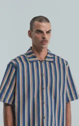 Camisa de manga corta con cuello abierto y calce oversize, confeccionada en sarga liviana a rayas verticales en tonos azul, amarillo y rojo.