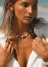 Collar corto con cuentas de nácar color beige y marrón, con dijes colgantes en forma de colmillos blancos.