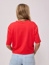 Remera gris de algodón con corte cropped y calce holgado. Tiene cuello redondo y mangas cortas con costuras reforzadas en color coral. Presenta un pequeño logo de la marca Rusty en el pecho.