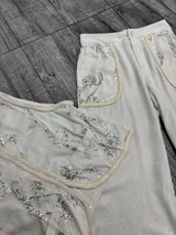 Conjunto de chaleco y pantalón color crudo con bordados de lentejuelas plateadas. El chaleco es sin mangas y el pantalón es de corte recto.