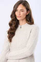 Campera tejida de abrigo color beige, con cierre frontal, cuello alto y bolsillos laterales.