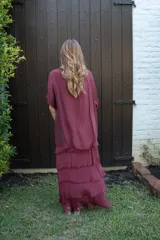 Vestido largo color cereza, con mangas amplias y escote en V. Presenta múltiples capas de tela con terminaciones deshilachadas, creando un efecto voluminoso y vaporoso.