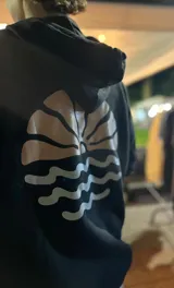 Hoodie color crema con estampado en la espalda de un sol naciente sobre el mar.