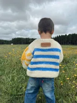 Sweater tejido de lana merino color crudo, con rayas horizontales azules y detalle de sol amarillo en una manga.