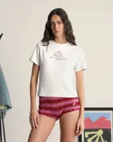 Remera color crema de algodón con cuello redondo y mangas cortas. Estampado en el centro del pecho con copas de vino y la frase "Más Vino Hahaha".