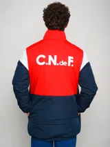 Campera parka de hombre con cuello alto, cierre frontal con cremallera y broches a presión, y escudo del Club Nacional de Football en el pecho. Diseño a bloques de color azul marino, blanco y rojo.