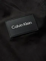 Sobrecamisa negra de sarga de algodón y nailon, corte boxy, cuello italiano, bolsillos con solapa en el pecho, billetera con botones, bajo recto, botones de gran tamaño e insignia con el logo de Calvin Klein en la manga.