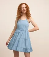 Vestido corto de jeans celeste, con breteles finos con lazos, escote en U, espalda descubierta y falda de tres niveles con volados.