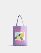 Bolso de tela color lila con asas cortas, estampado con dos limones y la palabra "lemon" en rosa.