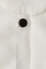 Blazer entallado color blanco con cuello redondo, cierre frontal con un botón visible y tapeta con botones ocultos. Tiene bolsillos delanteros ribeteados, abertura en los puños y pinzas moldeadoras adelante y atrás. Está forrado.