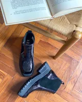 Botines negros de cuero con caña baja, puntera redondeada y cierre frontal con cremallera. Presentan paneles laterales de gamuza y suela track con plataforma.