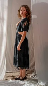 Vestido midi negro con estampado floral, escote en V profundo, mangas cortas abullonadas con encaje y aberturas laterales en la cintura.