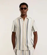 Camisa de manga corta confeccionada en tejido texturizado de algodón y poliéster. Presenta un diseño de rayas verticales en tonos beige, gris y mostaza, con cuello tradicional y cierre frontal de botones.