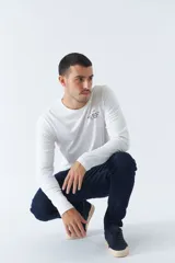 Remera blanca de manga larga con cuello redondo y estampado pequeño en el pecho.