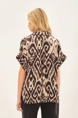 Camisa de corte amplio con estampado ikat en tonos beige y marrón. Tiene cuello camisero, manga corta y botones ocultos.