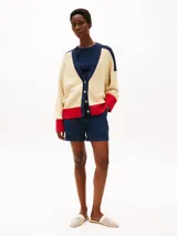 Cárdigan de punto color crema, con cuello en V, cierre con botones y corte amplio. Presenta detalles en azul marino en los hombros y en el borde del cuello, y detalles en rojo en los puños y en el ruedo. Logo de Tommy Hilfiger bordado en el pecho.