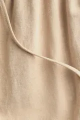 Pantalón de punto color beige, de corte holgado con piernas amplias, tiro alto, cintura elástica y cordón para ajustar.