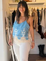 Musculosa celeste con breteles finos, escote en V y detalle de guarda calada con encaje en el ruedo. Tiene tres botones decorativos en el frente.