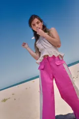 Pantalón de lino color fucsia, de tiro medio y corte holgado, con bolsillos laterales y franja vertical color crema en los laterales.