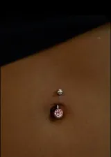 Piercing de ombligo en acero quirúrgico con dije de cristal rosa. La bolita superior es lisa, sin piedra.