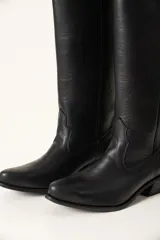 Bota texana alta de cuero negro con puntera fina y tachas plateadas en el borde superior.