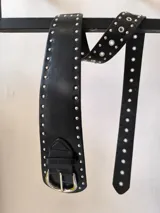 Cinturón ancho de cuero sintético negro con hebilla metálica plateada y doble hilera de tachas plateadas.