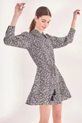 Vestido corto con estampado floral en blanco y negro, cuello camisero, mangas largas abullonadas y falda evasé con detalle de borlas.