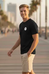 Remera negra de manga corta con cuello redondo y un pequeño parche circular con un diseño de palmera y sol en el pecho izquierdo.