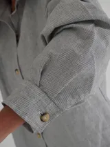 Camisa celeste a rayas verticales finas, con cuello clásico, cierre frontal con botones y mangas largas. Presenta bordados de un sol, un caballo y líneas horizontales en la parte superior de la espalda.
