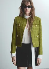 Chaqueta corta de tweed color verde oliva, con cuello redondo, cuatro bolsillos frontales y botones decorativos.