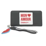 Billetera negra con textura símil cuero, cierre perimetral y tira de agarre con estampado a rayas blancas y negras. Presenta un aplique con la inscripción "Mon Amour" y un dije de labios.