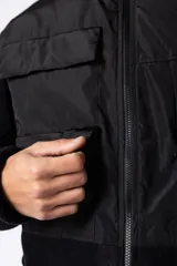 Campera negra con la parte superior de tela tipo rompevientos con dos bolsillos con solapa y la parte inferior de micro polar. Tiene cierre frontal y cuello alto.