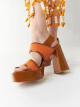 Sandalias de plataforma color naranja con detalles en marrón. Tienen tiras anchas sobre el empeine y el tobillo, y un tacón cuadrado alto.