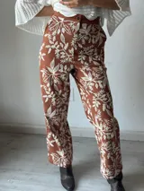 Pantalón de tela color terracota con estampado de hojas y flores en color blanco.