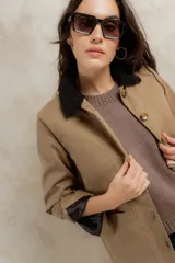 Campera color beige con cuello de corderito negro, cierre con botones, bolsillos laterales y puños con detalle de cuero sintético negro.