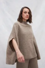 Poncho color crema de tejido de punto industrial con cuello alto y aberturas laterales para los brazos.