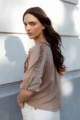 Blusa color beige de manga 3/4 confeccionada en algodón suave, con escote a la base y detalles de volados en 3D que recorren el frente, mangas y escote.