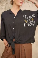 Camisa negra de lino con botones, corte clásico y mangas 3/4. Estampa frontal con la frase "Take it easy" en lentejuelas plateadas y corazones dorados.