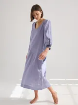 Vestido midi de lino color lila con escote en V y mangas 3/4 abullonadas con puño elástico. Presenta paneles laterales en denim y costuras a la vista en color rojo.