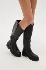 Bota alta de caña ancha color negro, con cierre lateral y detalle de hebilla ajustable en la parte superior de la caña. Suela de goma gruesa con relieve.