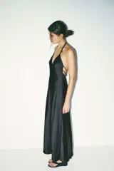 Vestido midi negro de satén con escote en V y tirantes finos. Detalle de tiras cruzadas en la espalda con lazadas. Cierre trasero con cremallera.