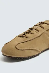 Zapatilla de cordones color negro, con capellada de cuero serraje, horma redonda y suela ultrafina.