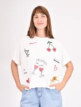 Remera blanca de corte holgado con mangas cortas y cuello redondo. Estampado con dibujos de cerezas, copas de vino, un leopardo y frases como 'Amore' y 'Salute!'.